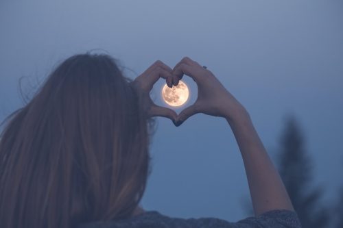 Woman making heart hands around full moon