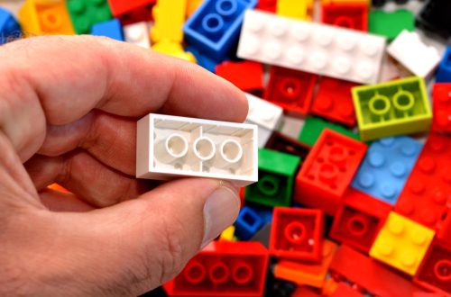 Mans hand holds a red toy block against mix of building blocks background. concept photo of imagination, creativity, planning and ideas.