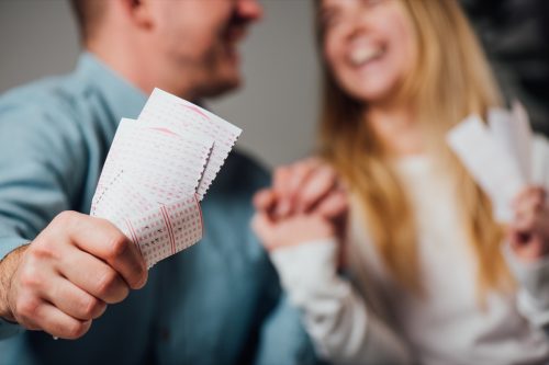 Happy man and woman holding hands while holding lottery tickets.