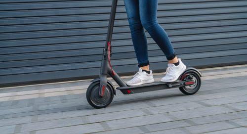 Close up of woman riding black electric kick scooter at cityscape.