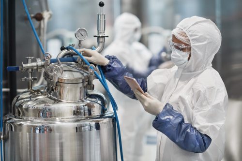 Portrait of female worker wearing protective suit while operating equipment at modern chemical plant