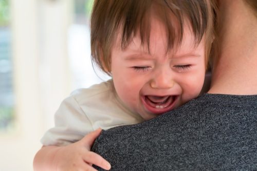 Upset toddler crying on parent's shoulder.