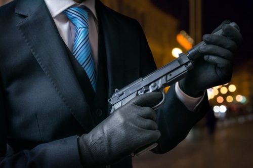 Hitman holds pistol with silencer in hands.