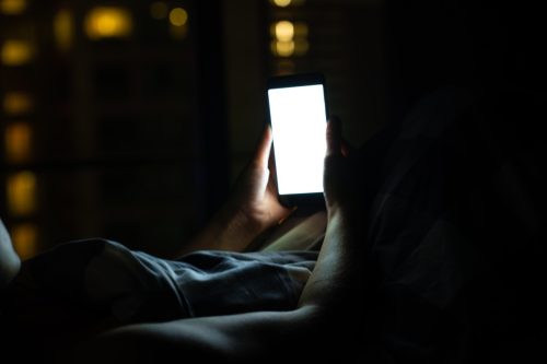 Woman on the bed before falling asleep looks at a smartphone