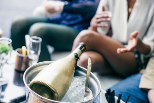 View of the golden champagne bottle in an ice bucket on the table in front of the seated people