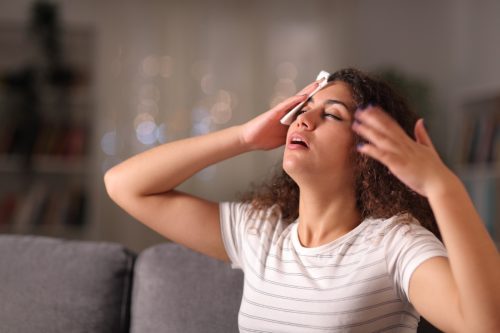 Stressed woman drying sweat in a warm night sitting on a couch in the living room at home