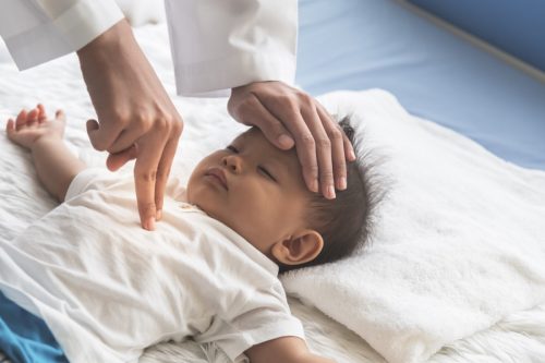 The doctor is using two fingers to press down in the middle of the baby's chest