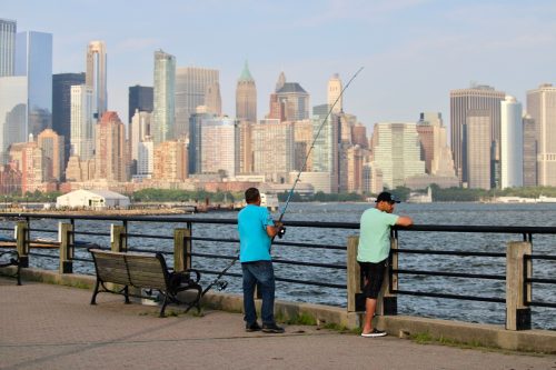 Two Fishermen are fishing into the Hudson River from the pier in front of the Manhattan Skyline 
