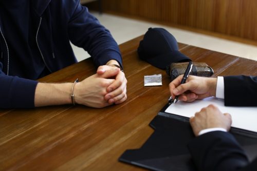 Police officer interrogating criminal in handcuffs at desk indoors