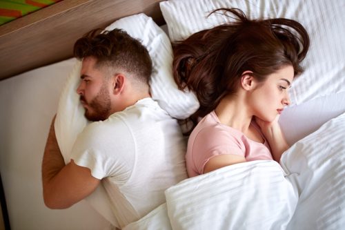 Couple lying in bed drifting apart