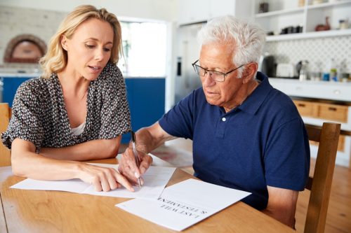 Woman Helping Senior Man To Complete Last Will And Testament At Home