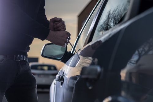 Auto thief in black balaclava trying to break into car with screwdriver. 