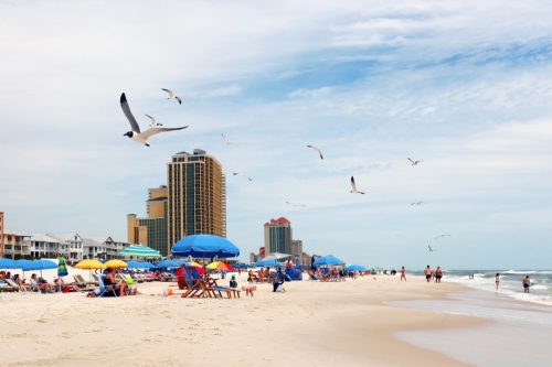 Alabama Gulf of Mexico beach life. Marine landscape with beach line homes and hotels, beach umbrellas, people and flying birds on a foreground. Alabama Gulf Shores State park and beach, USA.