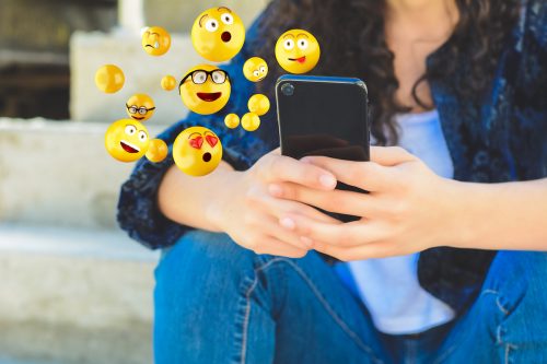 Close-up of woman using smartphone sending emojis.