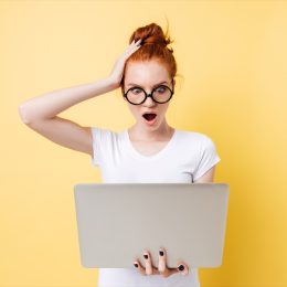 shocked woman with red hair holding a laptop against an orange background