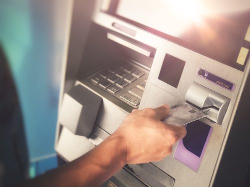 Man's hand inserting ATM credit card into bank machine to transfer money or withdraw - Image