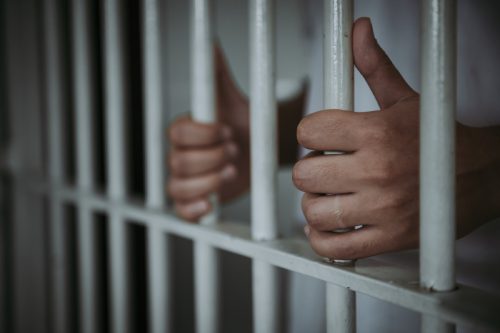 close up of hands holding bars in prison