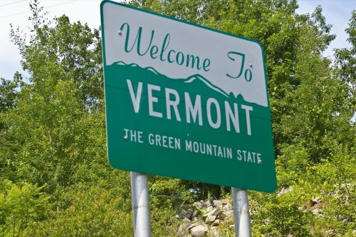 a green "Welcome to Vermont" sign in front of green trees