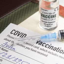 A COVID-19 vaccination record card with a vile of vaccine and a syringe.