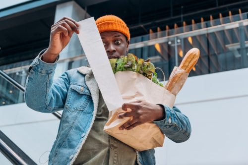 man holding groceries looking surprised at receipt