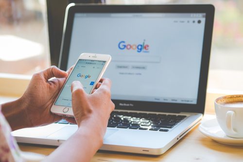 A close up of someone's hands using a phone and a laptop to access Google