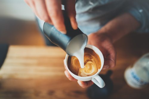 Closeup of a barista pouring milk into a coffee drink