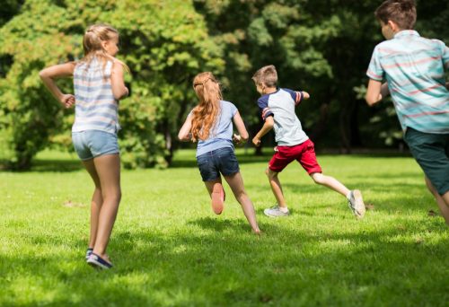 Group of happy kids or friends playing catch-up game and running in summer park.