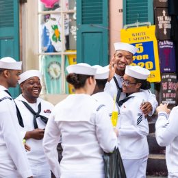 Old town street in Louisiana city with happy people sailors group holding drinks talking on sidewalk during Navy Week.