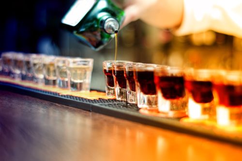 Bartender pouring strong alcoholic drink into small glasses on bar, shots