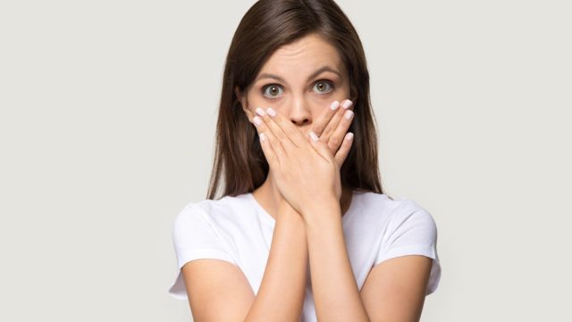 Woman in white t-shirt cover mouth with hands.