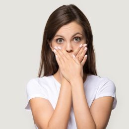 Woman in white t-shirt cover mouth with hands.