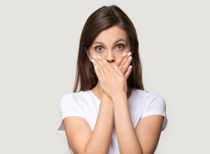 Woman in white t-shirt cover mouth with hands.