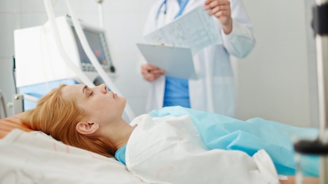 Unconscious woman lying on bed in hospital with doctor standing nearby.