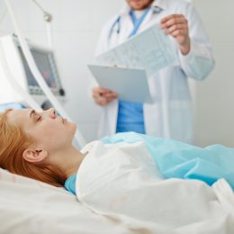 Unconscious woman lying on bed in hospital with doctor standing nearby.