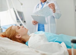 Unconscious woman lying on bed in hospital with doctor standing nearby.