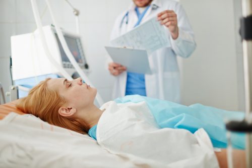 Unconscious woman lying on bed in hospital with doctor standing nearby.