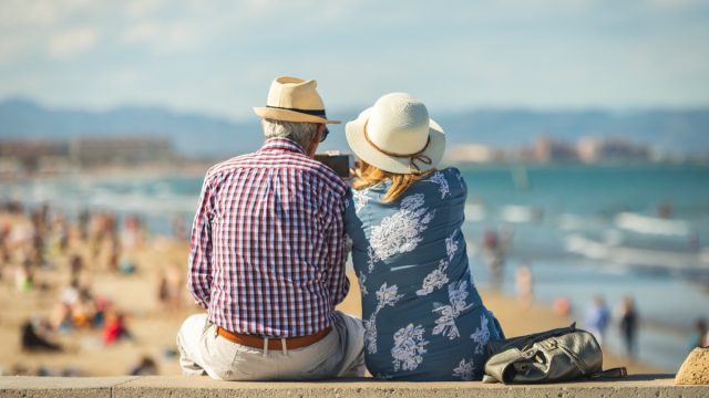 Mature couple of retired lovers enjoying retirement on the beach facing the sea with mobile cell phone taking pictures at sunset