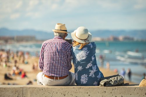 Mature couple of retired lovers enjoying retirement on the beach facing the sea with mobile cell phone taking pictures at sunset