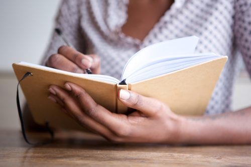 Close up partial portrait of a female author at home writing in journal.