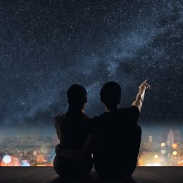 Silhouette of couple sit on ground point faraway on the roof above the city in the night.