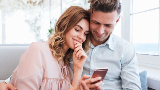 Family portrait of happy couple man and woman resting in restaurant and watching on mobile phone together on date