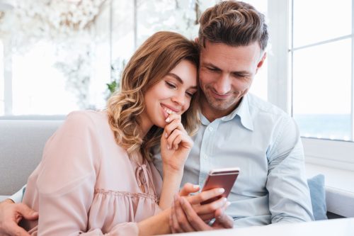 Family portrait of happy couple man and woman resting in restaurant and watching on mobile phone together on date