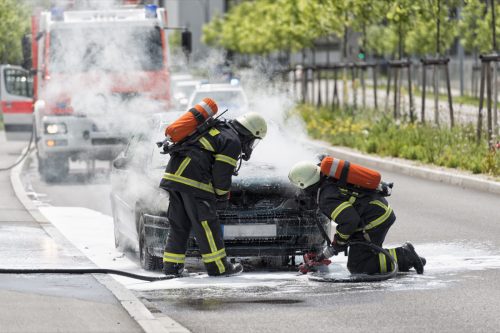 Burning motor vehicle been put out by firemen in protective clothing