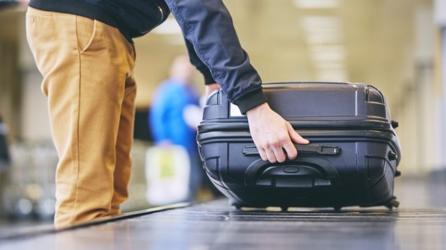 Traveler,Picking,Up,Suitcase,From,Baggage,Claim,In,Airport,Terminal.