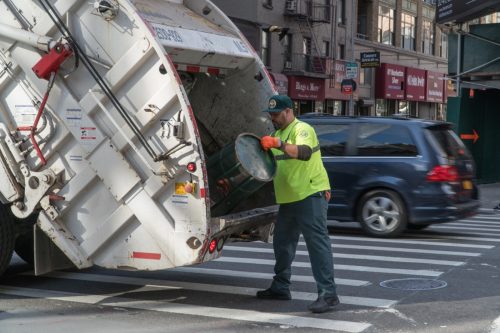 Sanitation department workers empty trash can into garbage truck to keep street clean