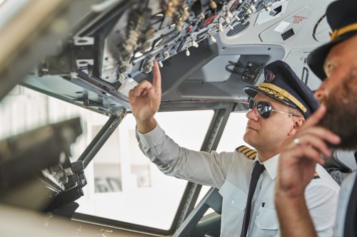 Pilot in sunglasses pushing the buttons on the dashboard plane while working in a cockpit with colleague