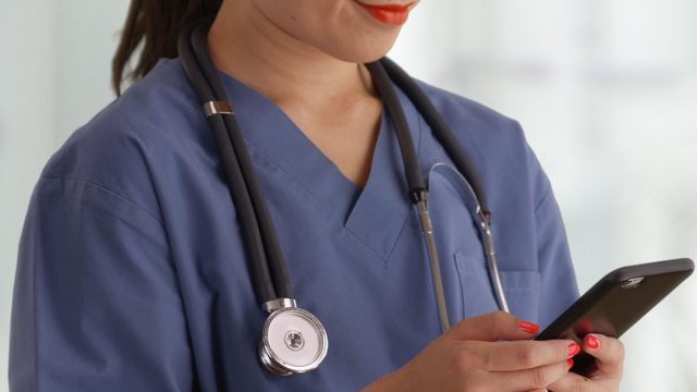 Happy,Young,Asian,Doctor,In,Scrubs,Texting,With,Smartphone,Inside