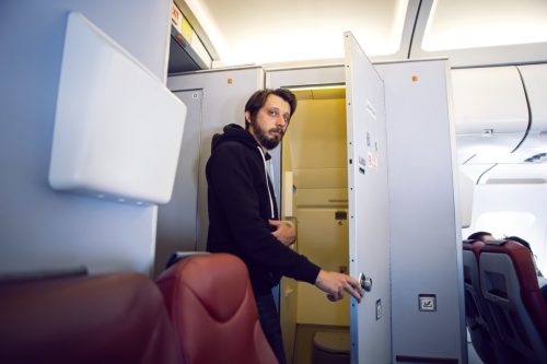 Man in black clothes goes to the toilet on the plane.