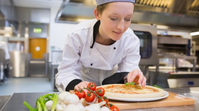 Woman preparing pizza in kitchen.