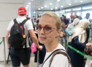 Young blond caucasian woman waiting in long line at security check at the departure airport terminal. Lady standing in long queue at airport before boarding a plane.